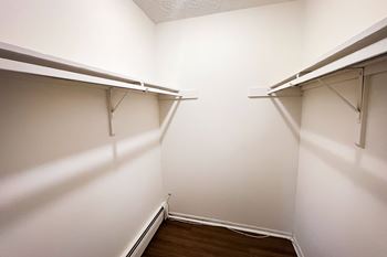 Empty white closet with shelves and a wooden floor.